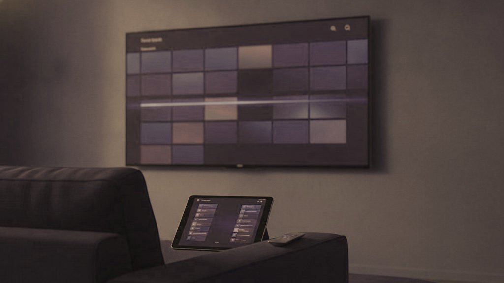 A TV showing a programme guide grid with a tablet and phone showing channel lists on a sofa