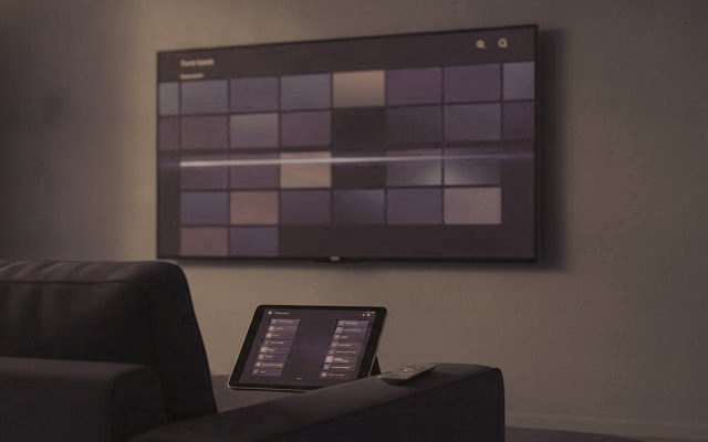 A TV showing a programme guide grid with a tablet and phone showing channel lists on a sofa
