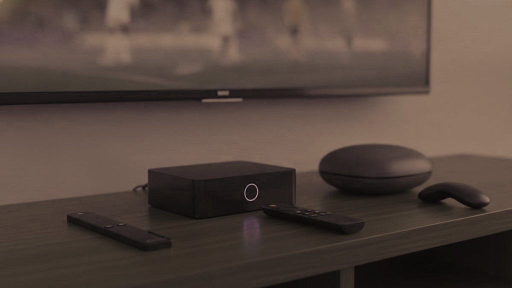 A streaming stick, a set-top box and a round streaming box with their remotes on a TV console