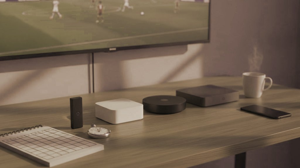 Five streaming devices, a notebook scoring grid and a stopwatch in front of a TV showing a football match