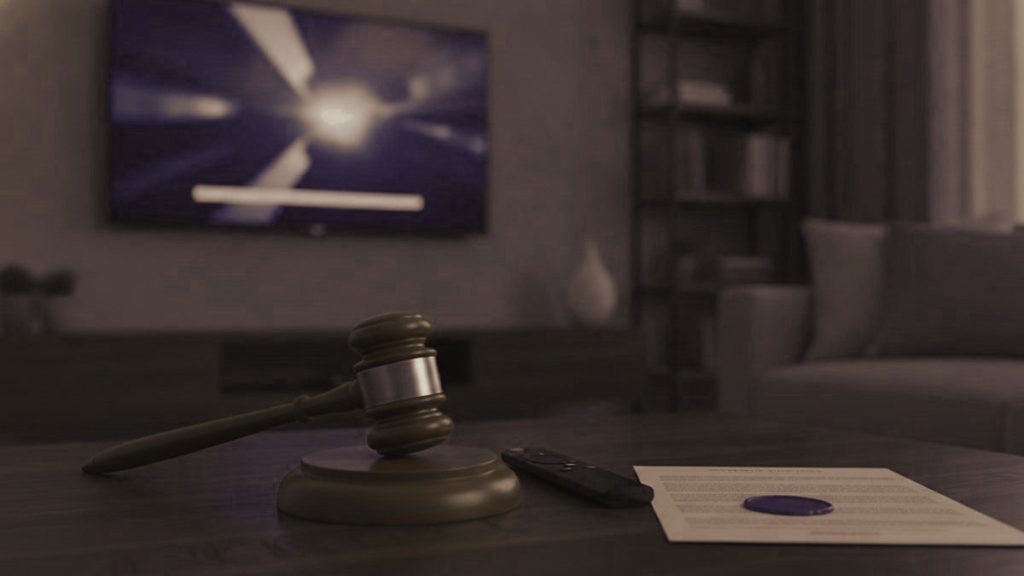 A judge gavel, a streaming remote and a sealed document on a coffee table in front of a TV