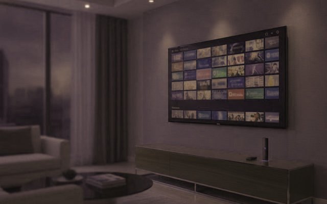 A living-room TV showing an IPTV channel guide with a streaming stick on the console